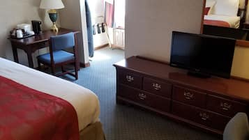 A hotel room with a large bed, a desk with a lamp, a television, and a dresser.