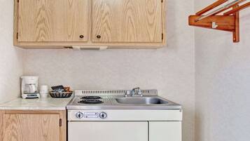 Una kitchenette compacta con un mueble de madera, estufa integrada, pileta y cafetera.