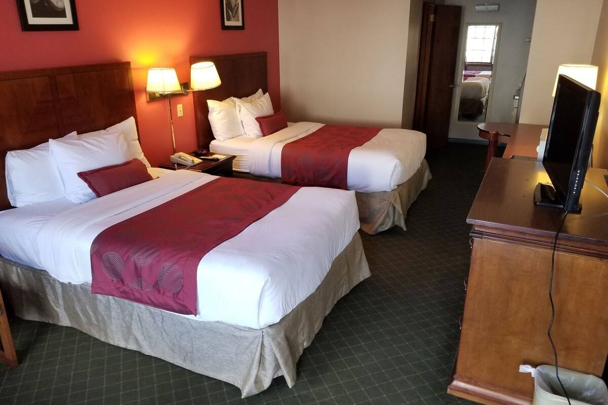 Quarto de hotel com duas camas, uma secretária com televisão e um espelho.