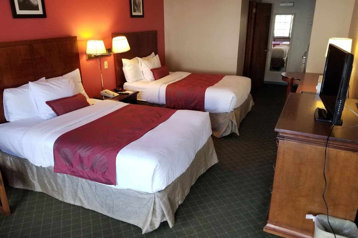 Quarto de hotel com duas camas, uma secretária com televisão e um espelho.