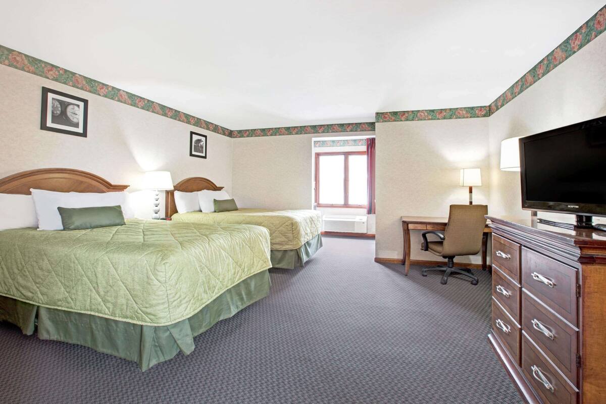 Quarto de hotel com duas camas, uma escrivaninha, uma televisão e uma janela com cortinas.