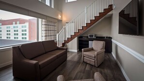 Een woonkamer met een bruine bank, een gestreept fauteuil en een houten trap.