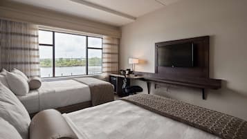 Een hotelkamer met twee bedden, een bureau, een televisie en een raam met uitzicht op een brug en groen.