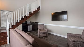 A living room with a staircase, a flat-screen TV, a microwave, and a kitchenette.