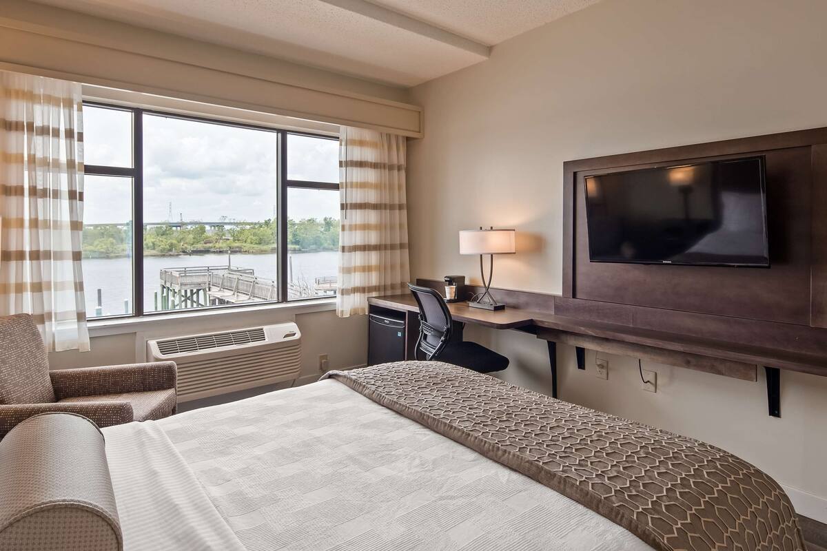 Une chambre d’hôtel avec un lit, un bureau, une chaise, une télévision et une fenêtre avec des rideaux.