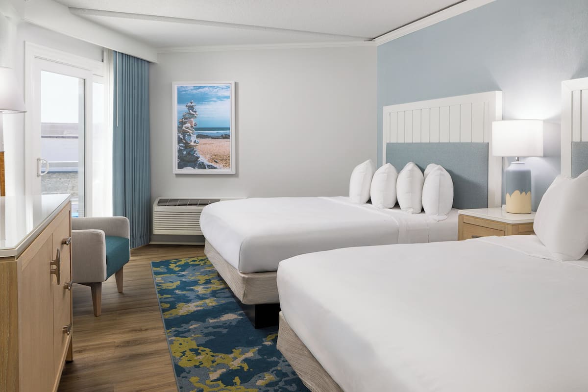 Ein Hotelzimmer mit zwei Betten, einem Schreibtisch, einem Stuhl, einem Fenster mit Vorhängen, einem Gemälde und einer Lampe.
