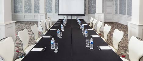 A conference room with a long table, white chairs, water bottles, and a projector screen.