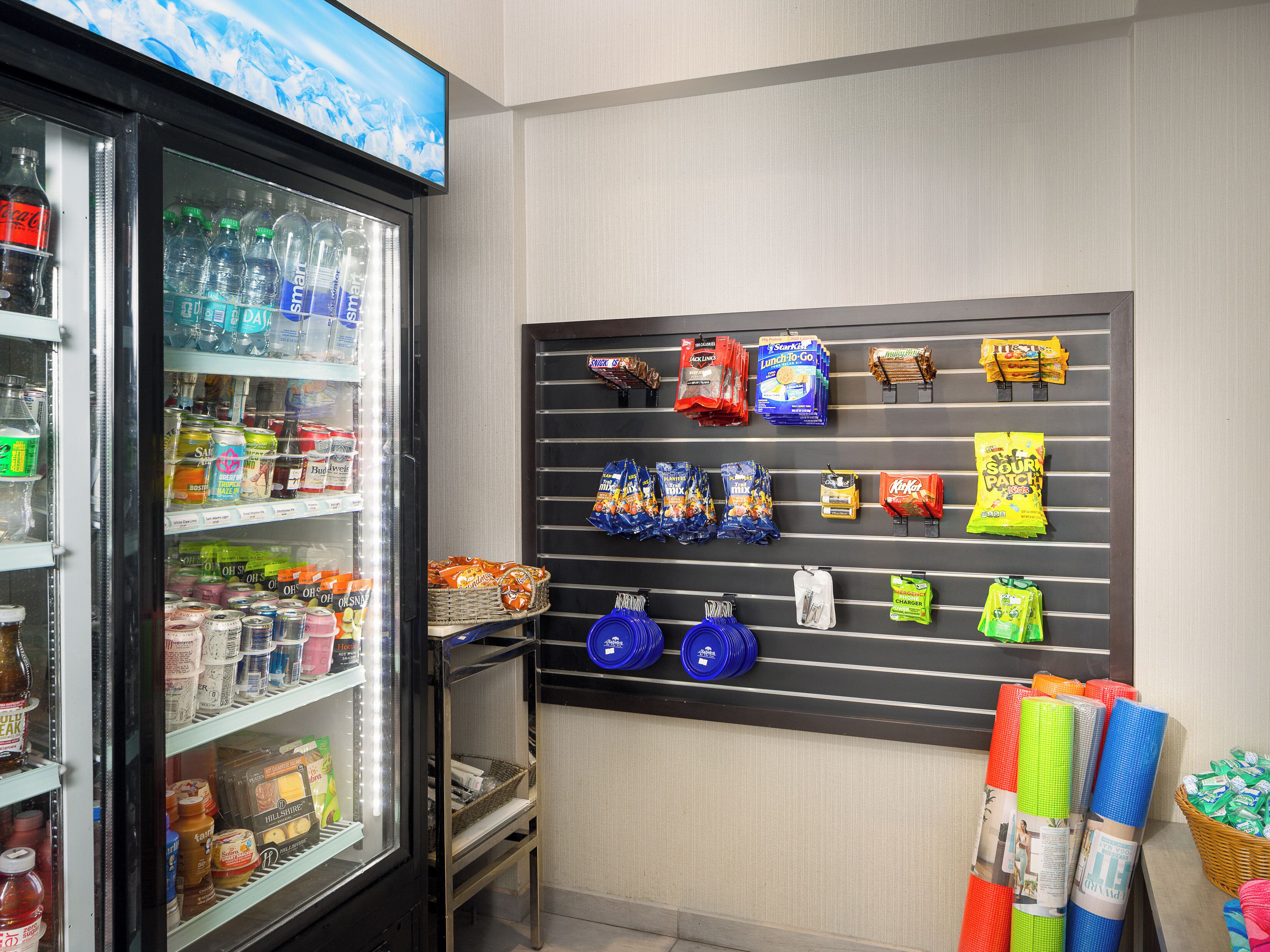 A vending machine stocked with beverages and snacks, a wall-mounted display of various packaged goods, and a basket with rolled-up items.