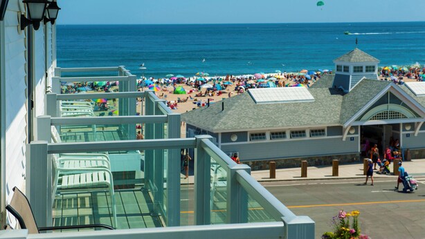 A beachside hotel with a balcony overlooking the ocean, a pool area, and a beach with umbrellas. - Ashworth by the Sea (Hampton)