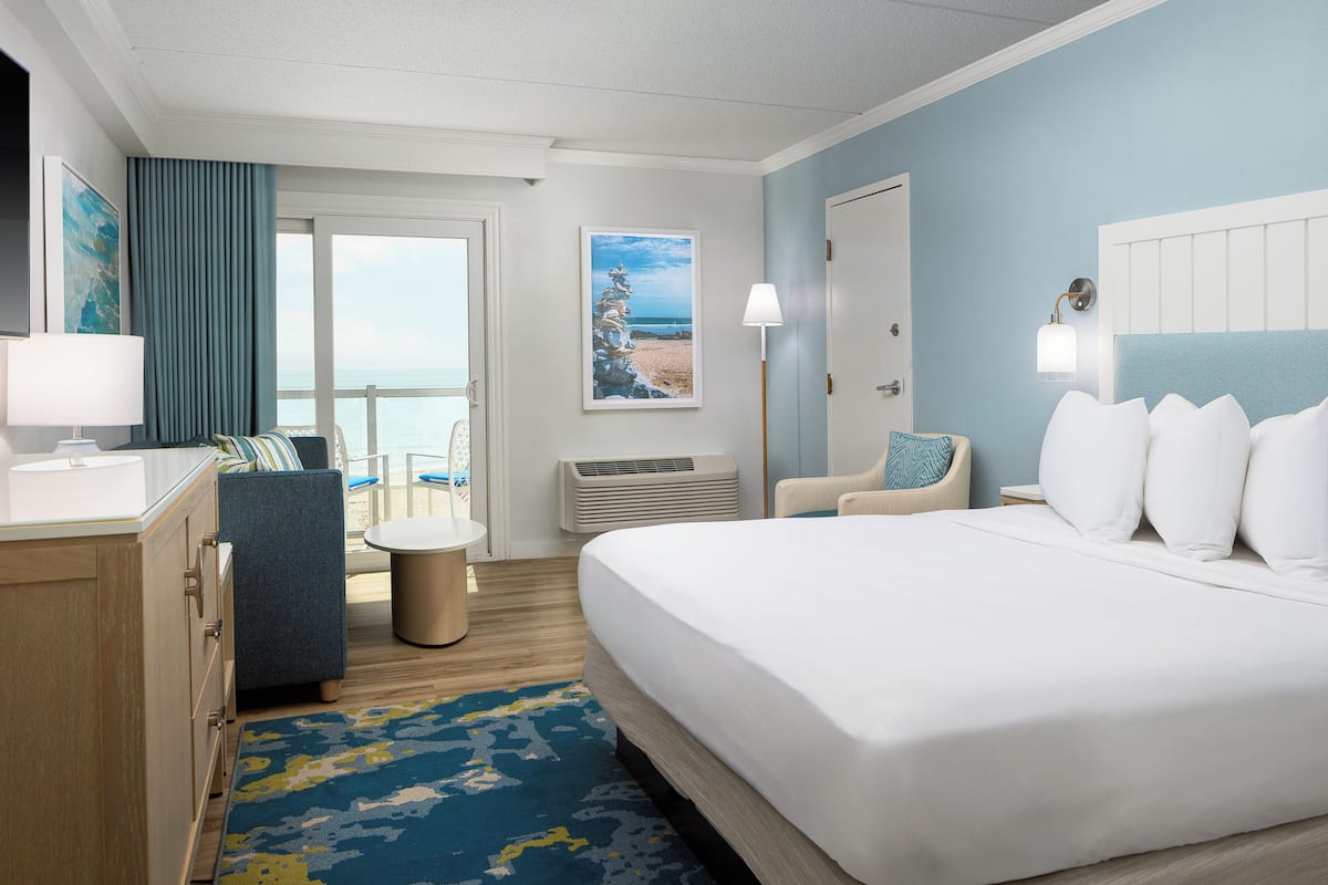Ein Hotelzimmer mit Bett, Schreibtisch, Stuhl, Lampe und Meerblick.