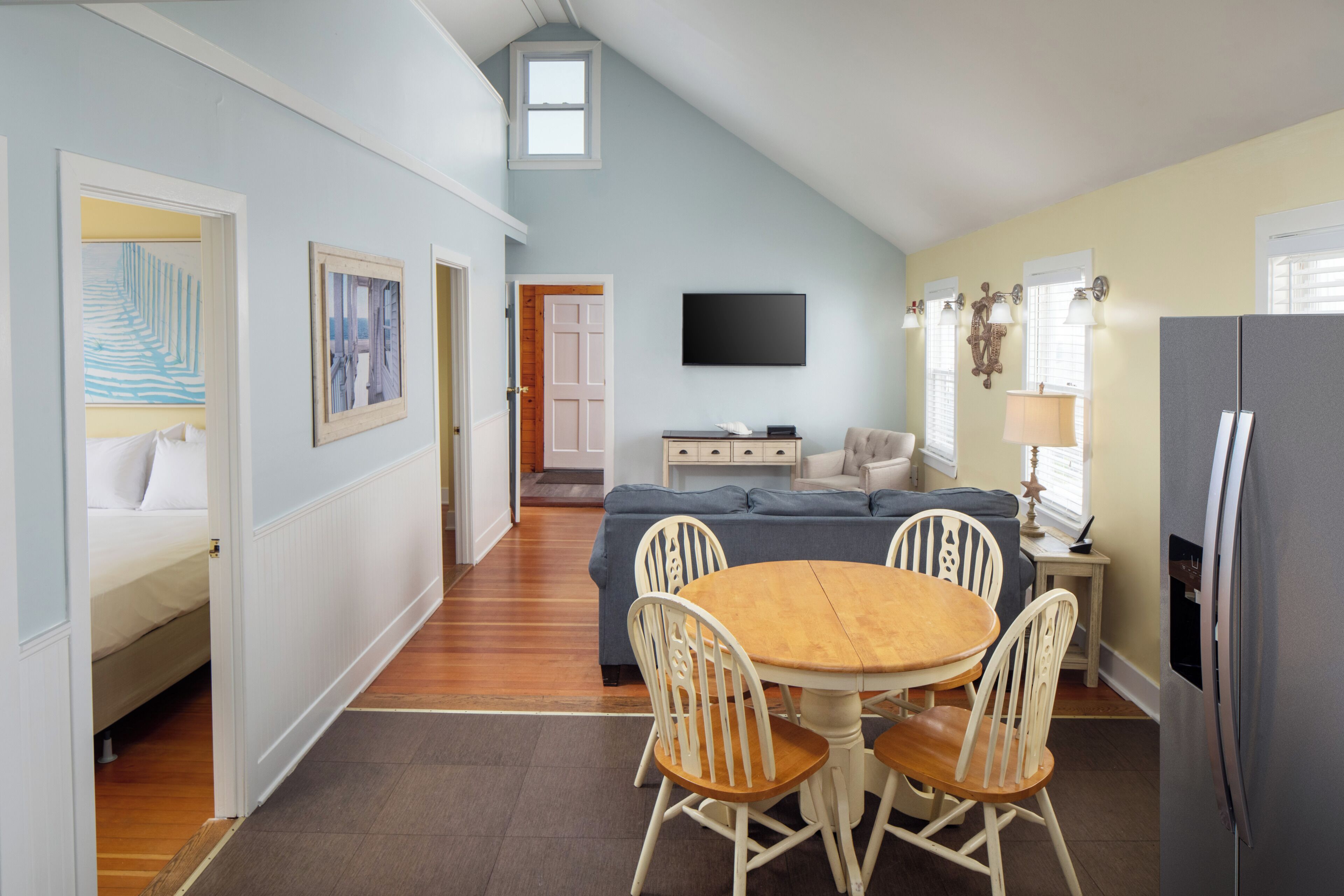 A dining area with a round table and chairs, a sofa, a television, and a refrigerator.