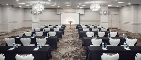 A conference room with rows of tables and chairs, water bottles, and a projector screen.