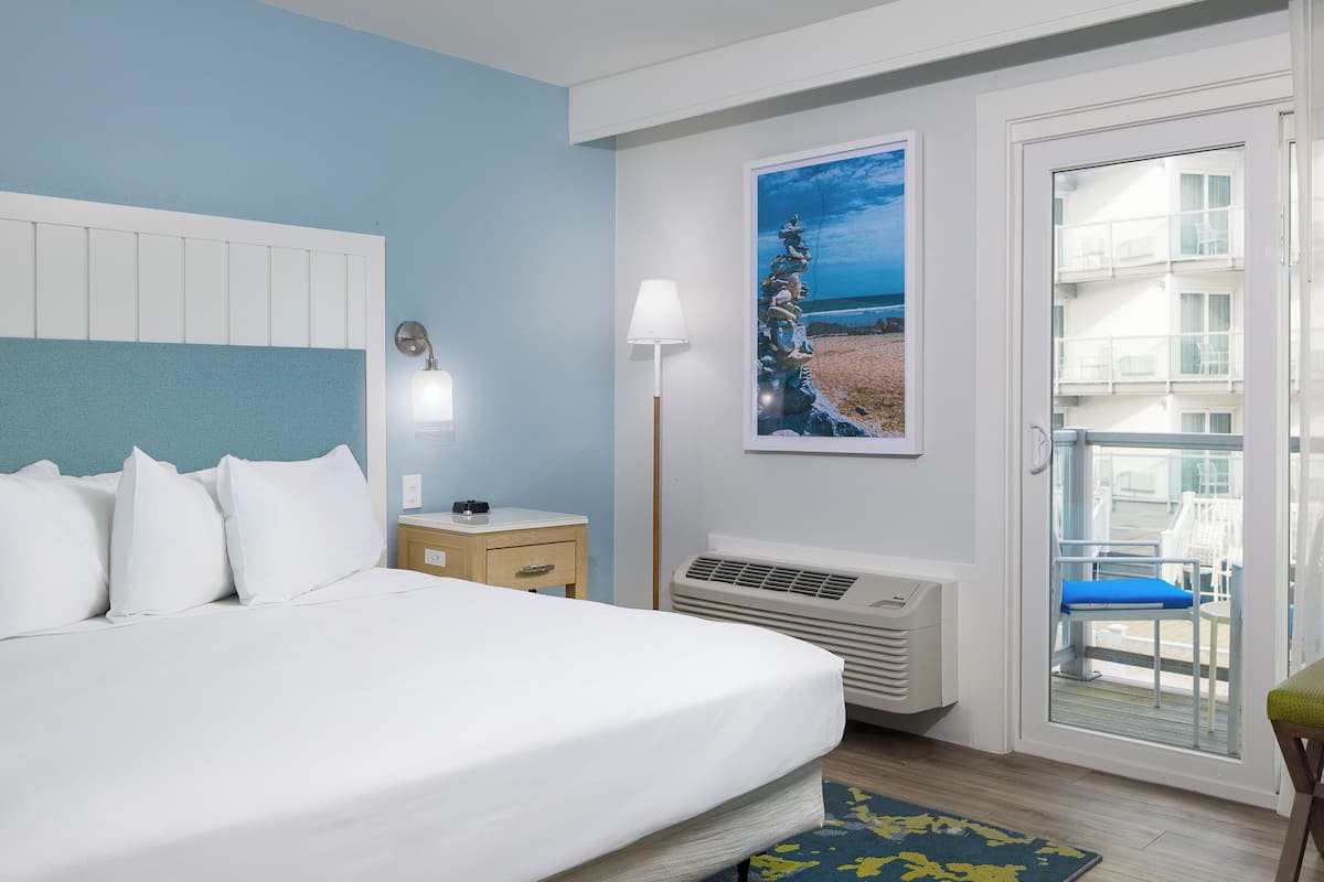 Ein Hotelzimmer mit Bett, Nachttisch, Lampe, Klimaanlage und einem Balkon mit Stühlen.