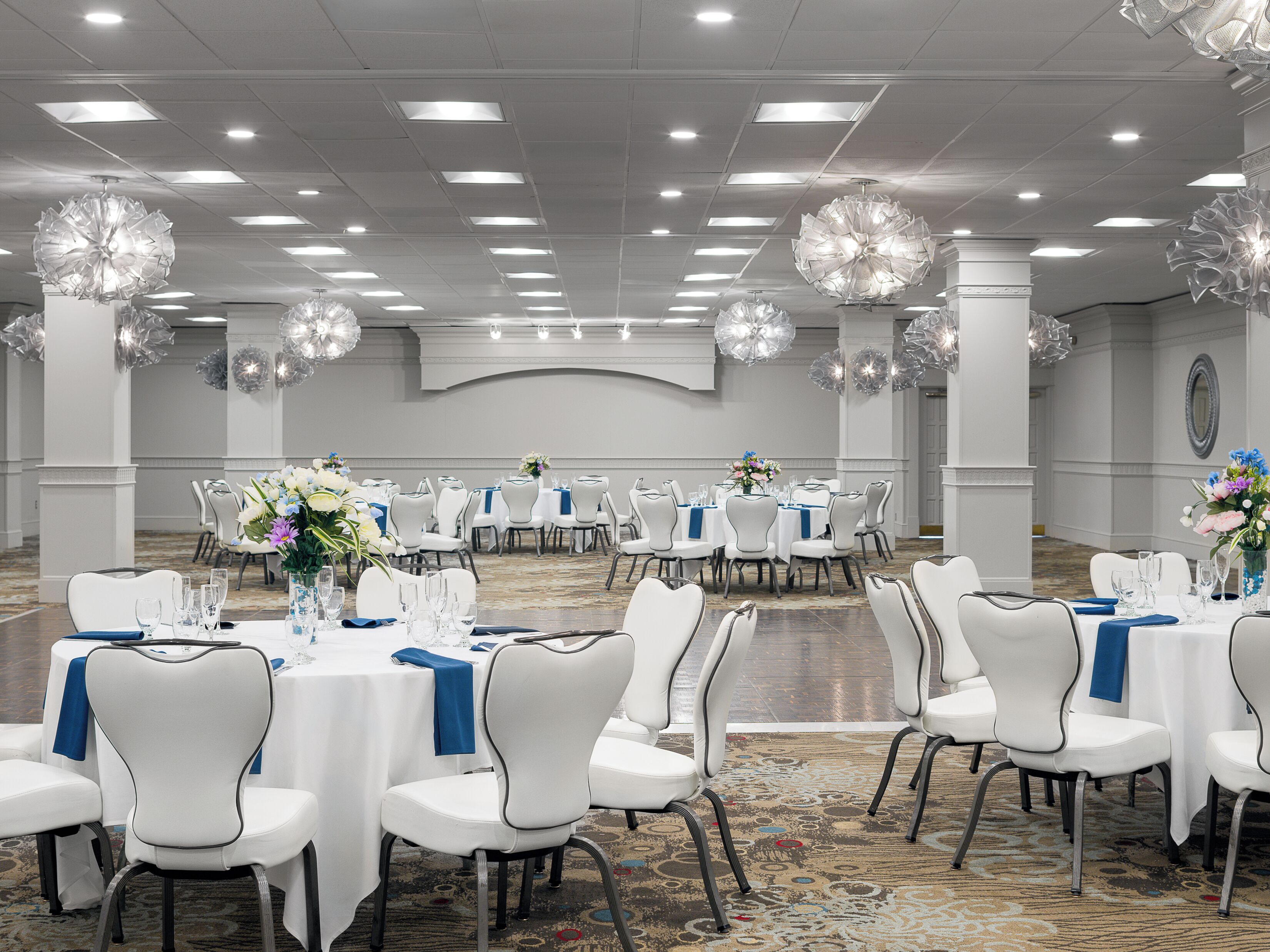 A banquet hall with round tables, white chairs, and blue tablecloths.