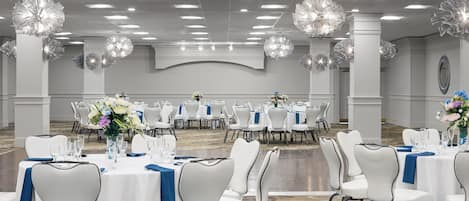 A banquet hall with round tables, white chairs, and blue tablecloths.