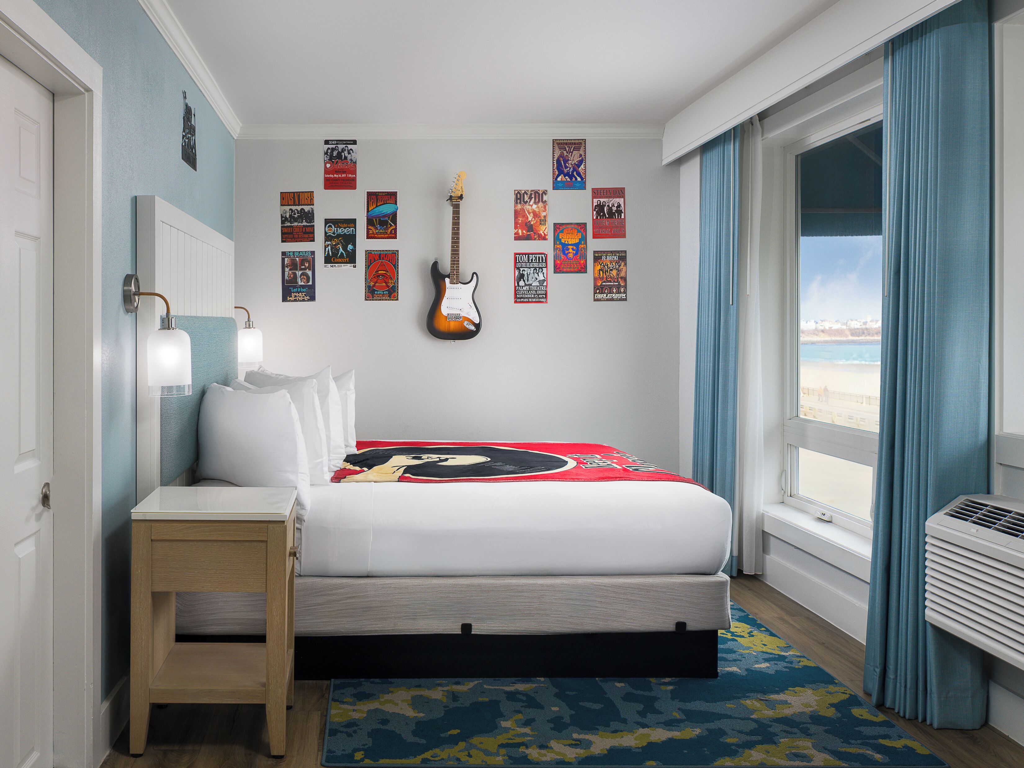 Une chambre à coucher avec un lit, une guitare, des affiches sur les murs, une table de chevet et une fenêtre avec des rideaux.