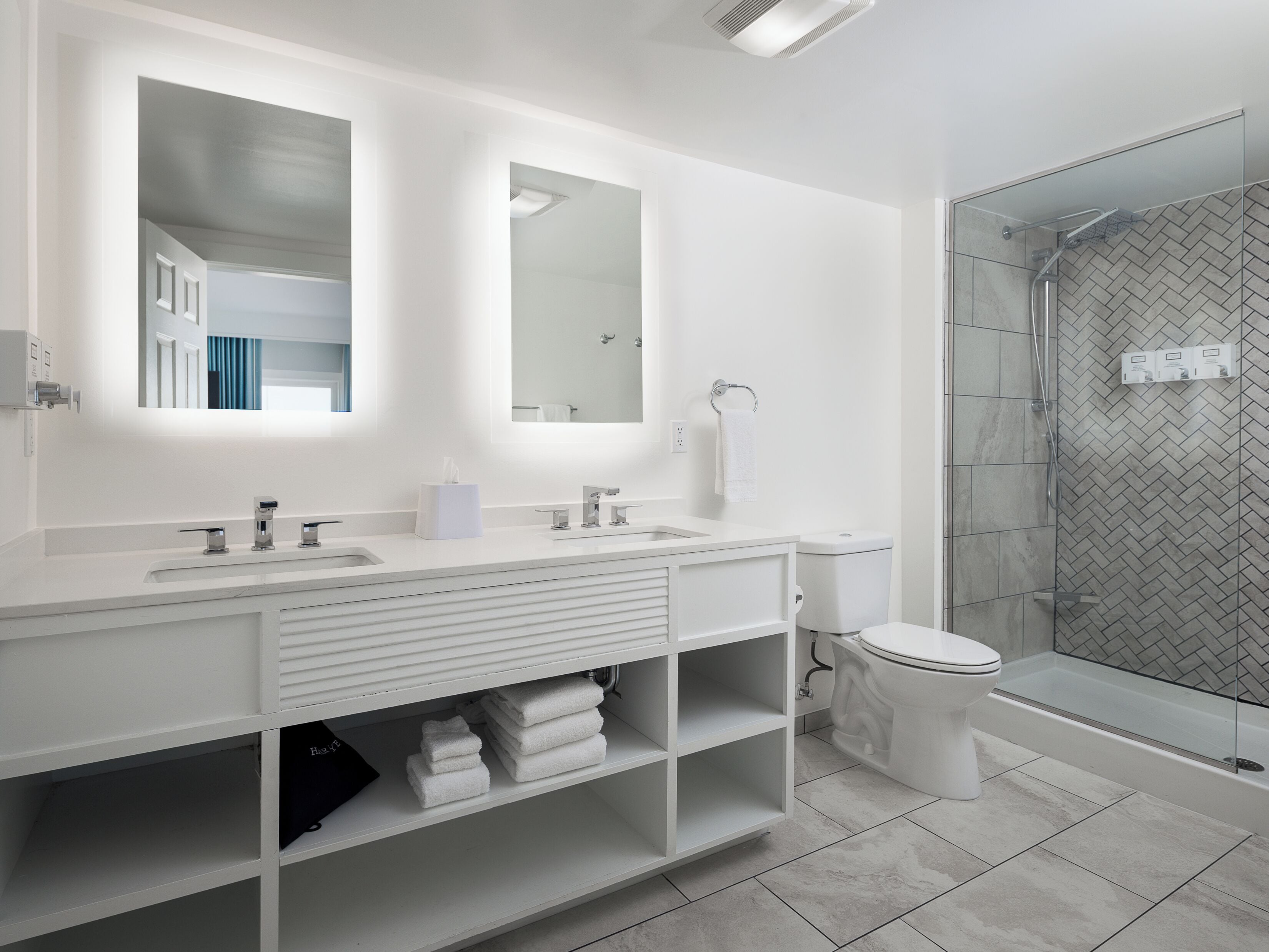 A modern bathroom with a white vanity, a large mirror, a glass shower enclosure, and a toilet.