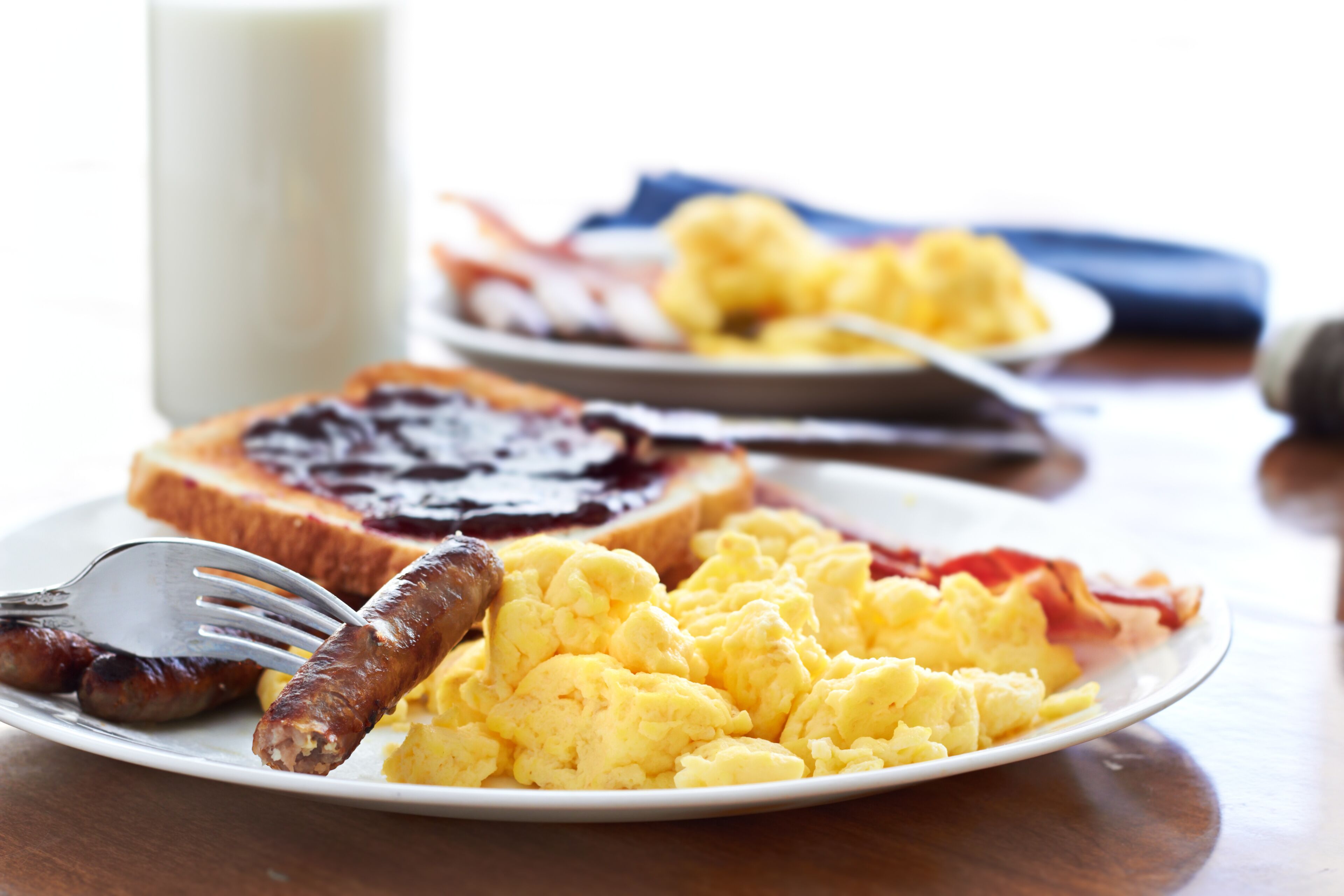 A breakfast plate with scrambled eggs, bacon, sausage, and jam on toast.