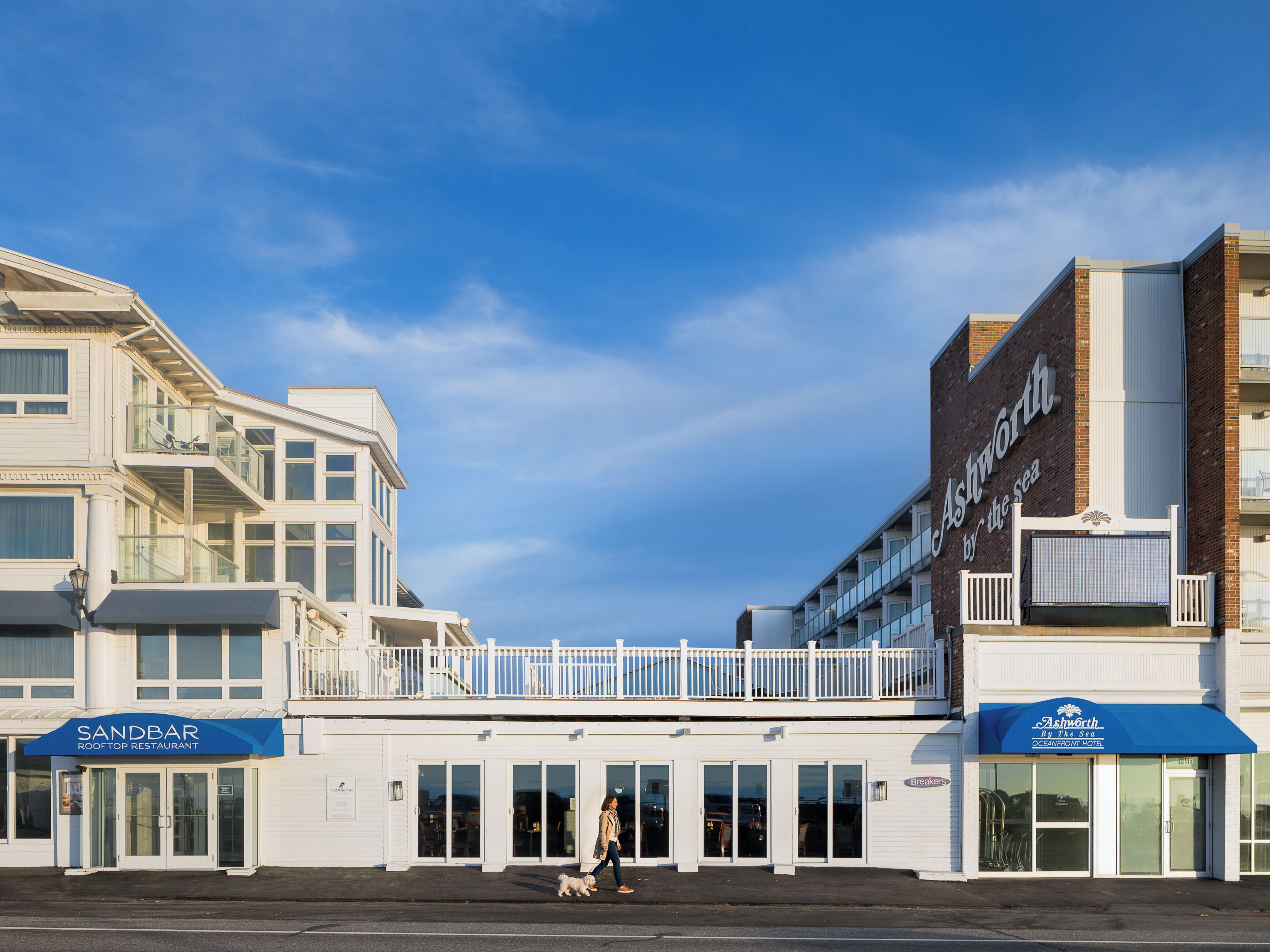 A beachfront hotel with a prominent sign, a pedestrian walkway, and a view of the sea.
