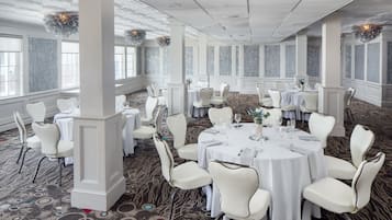 A banquet hall with round tables, white chairs, and a patterned carpet.