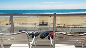 A balcony with a view of the beach and ocean. There are several cars parked in the foreground. - Ashworth by the Sea (Hampton)