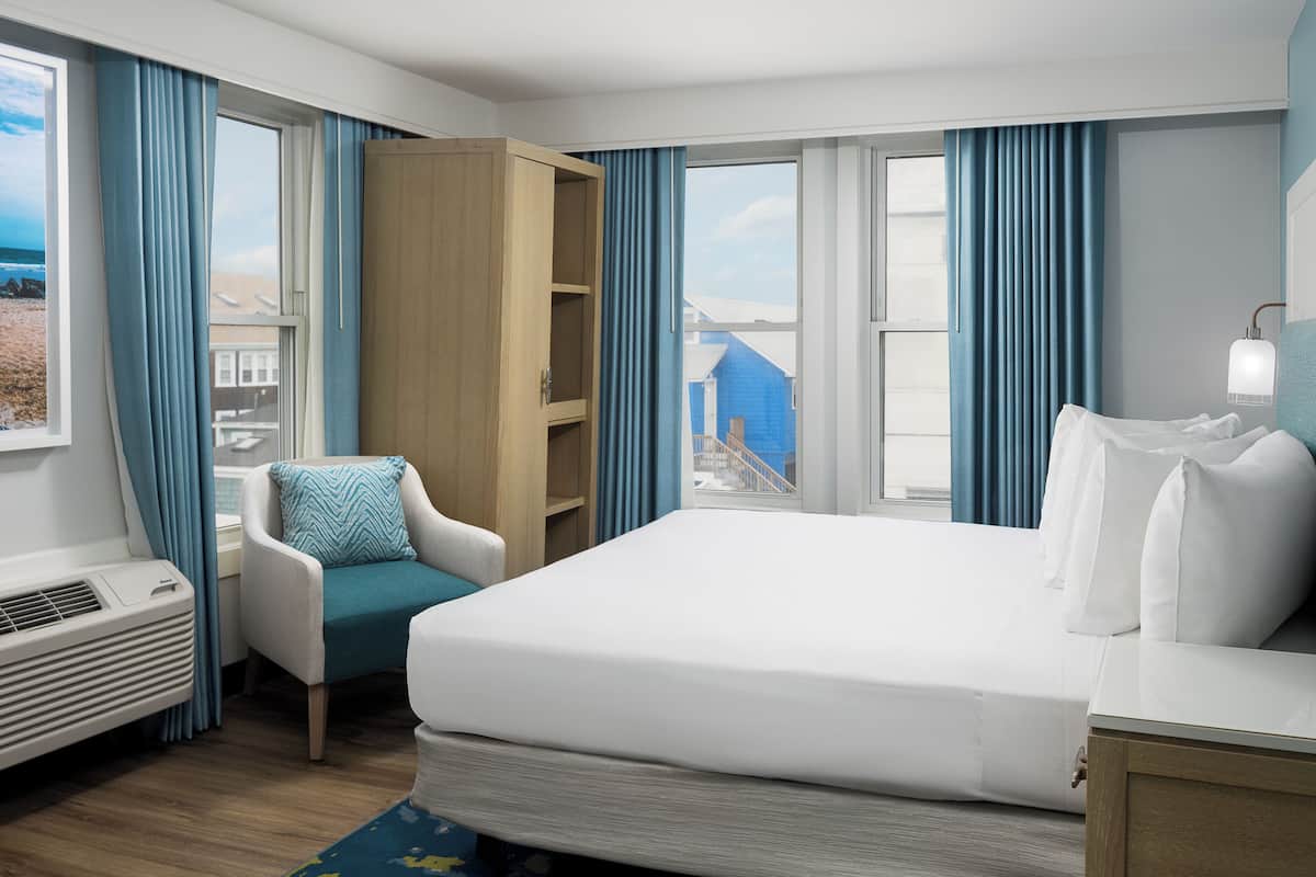 Ein Hotelzimmer mit Bett, Stuhl, Schreibtisch, Kleiderschrank und Blick auf den Strand.