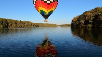 A hot air balloon over a calm lake with a forested shoreline.