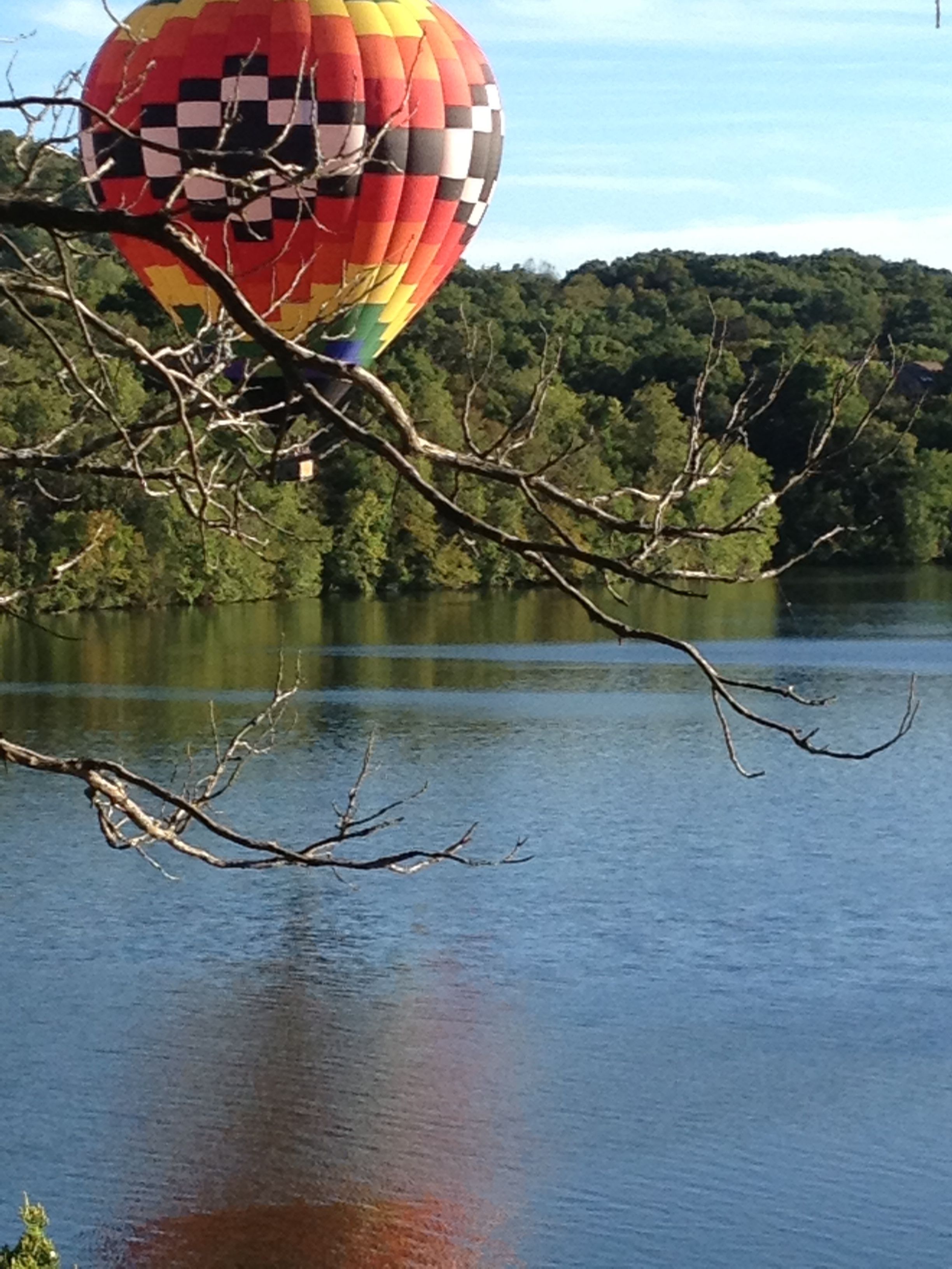 A hot air balloon with a checkered pattern over a body of water with trees in the background.