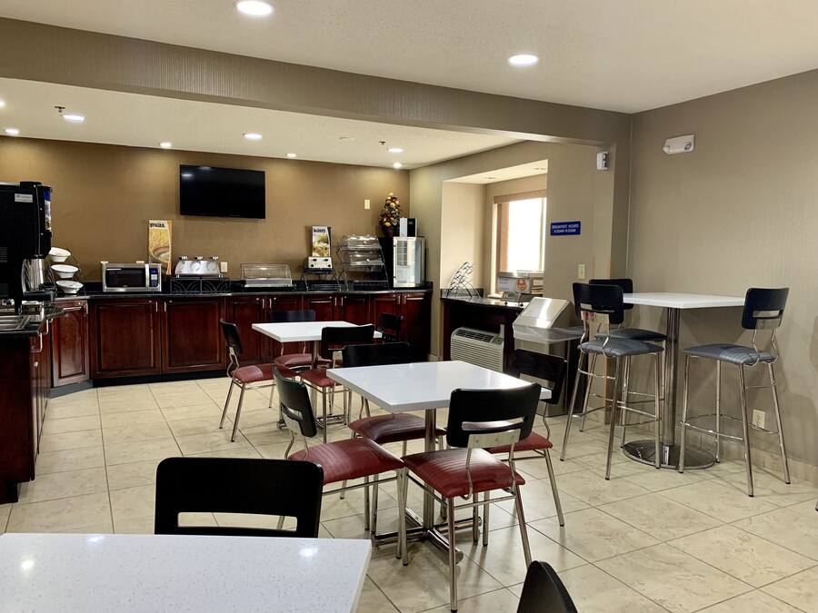 Una cafetería limpia y bien iluminada con televisor de pantalla plana, mesa de buffet y zona de estar con mesas y sillas.