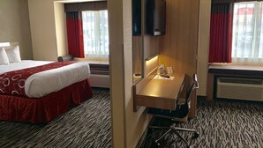 Une chambre d’hôtel avec un lit, un bureau, une chaise, une télévision et une fenêtre avec des rideaux.