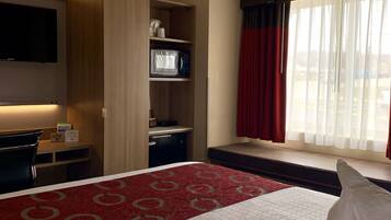 A hotel room with a bed, a desk, a microwave, and a TV.