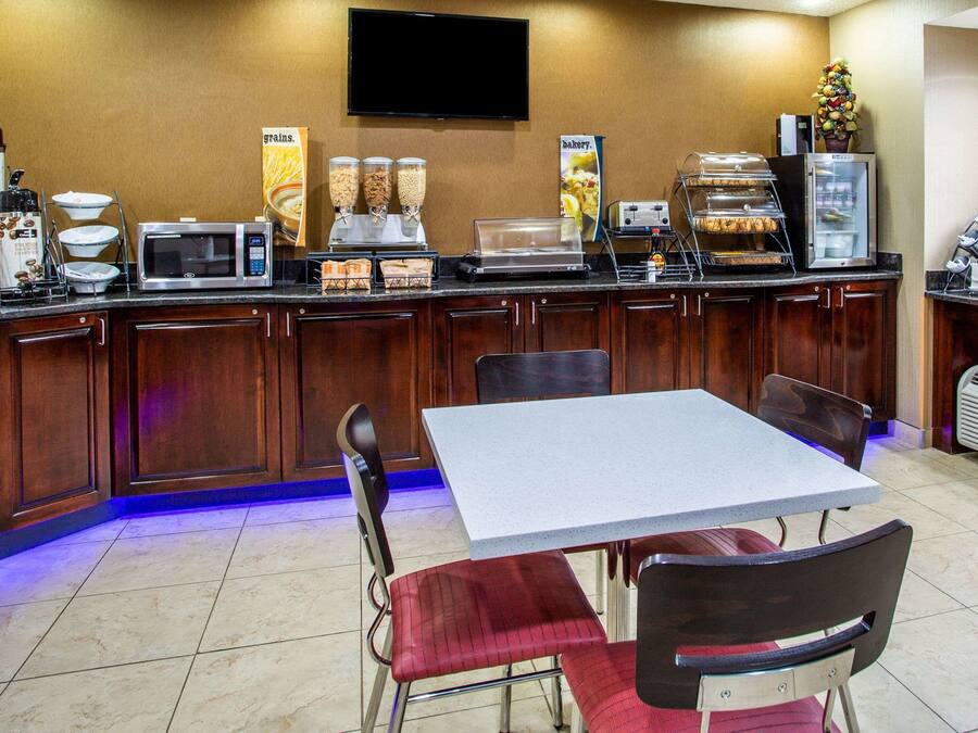 Una barra de desayuno con microondas, cafetera y dispensadores de cereales. Hay una mesa con sillas y un televisor montado en la pared.
