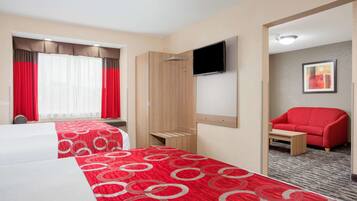 Ein Hotelzimmer mit zwei Betten, einem Fernseher, einem roten Sessel und einem kleinen Tisch.