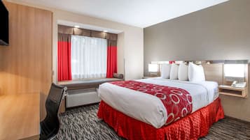 A hotel room with a bed, a desk, a chair, a TV, and a window with curtains.