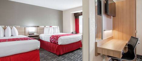 A hotel room with two beds, a desk with a chair, a TV mounted on the wall, and a window with red curtains.