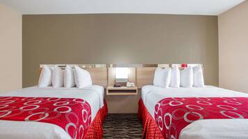 A hotel room with two beds, each with white bedding and red accents, a small bedside table with a lamp, and a mirror above the bed.