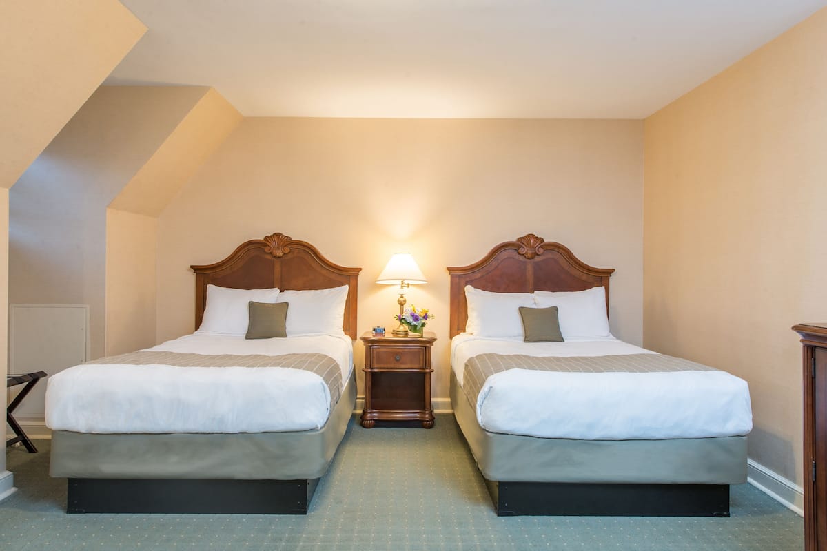 A hotel room with two beds, a nightstand with a lamp, and a small table with flowers.