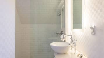 Une salle de bain avec un lavabo blanc, une cabine de douche en verre et un miroir.