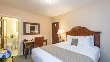 Ein Hotelzimmer mit einem großen Bett, einem Holztisch, einem Stuhl, einem Spiegel und einem durch eine offene Tür einsehbaren Badezimmer.