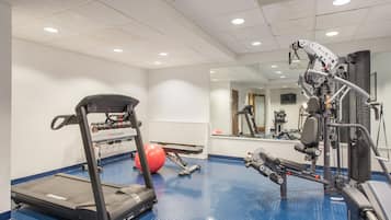 Une salle de sport équipée de matériel d’exercice, d’un tapis de course et d’un ballon rouge.