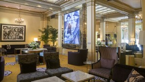 A spacious lobby with a high ceiling, chandeliers, a large screen, and comfortable seating areas.