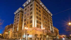 A multi-story hotel with a classic architectural design, featuring a prominent entrance with an American flag, large windows, and a well-lit facade.