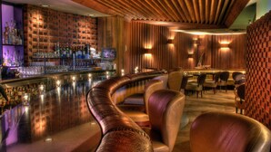 A bar area with a curved seating arrangement, a brick wall with shelves of bottles, and a wooden ceiling.