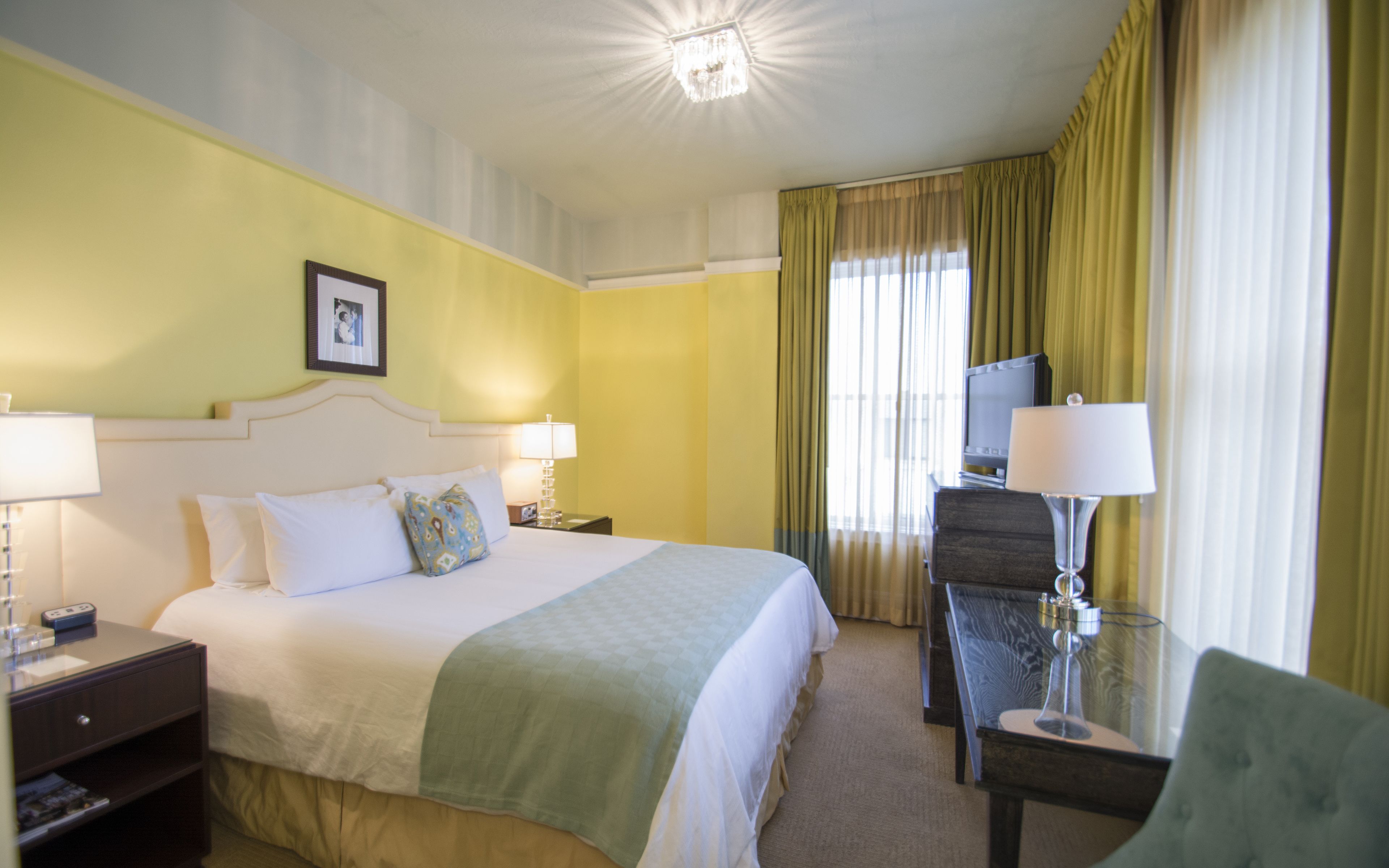 Une chambre d’hôtel comprenant un lit, des tables de chevet, un bureau avec une chaise, une télévision et des rideaux.