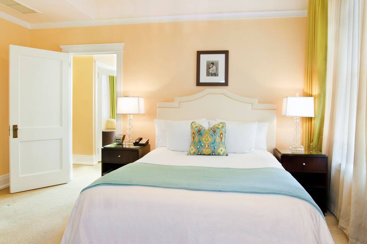 Habitación de hotel con una cama grande, dos mesitas de noche, una mesilla auxiliar, una puerta y un aplique en el techo.