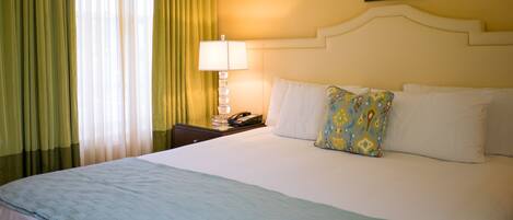 A hotel room with a bed, a nightstand with a lamp, a framed picture on the wall, and curtains.