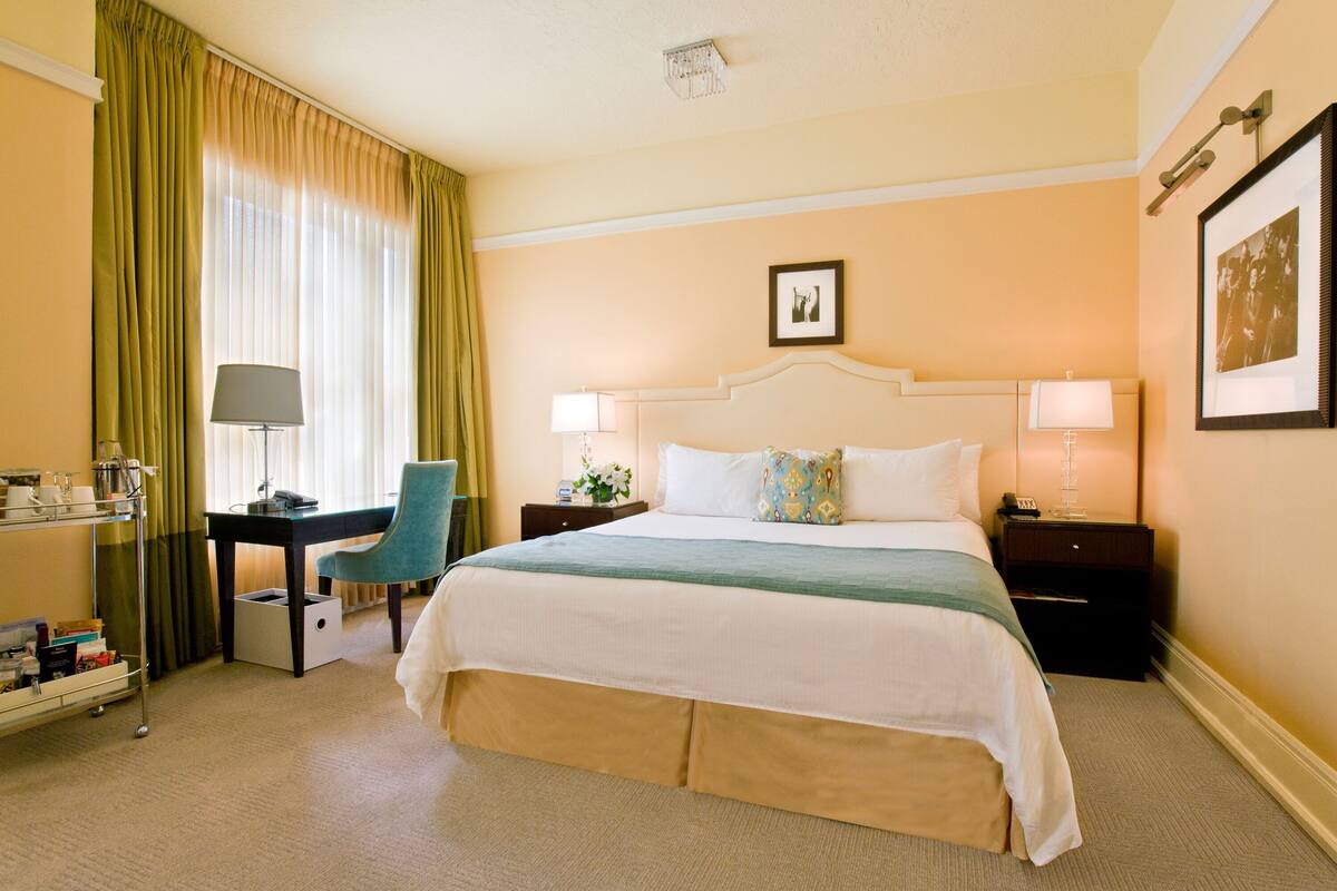 Habitación de hotel con una cama grande, un escritorio, una silla, una mesita de noche y una lámpara.