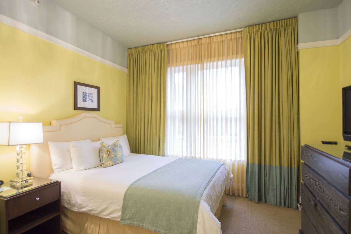 Una habitación de hotel con una cama, un aparador, un televisor y una ventana con cortinas.