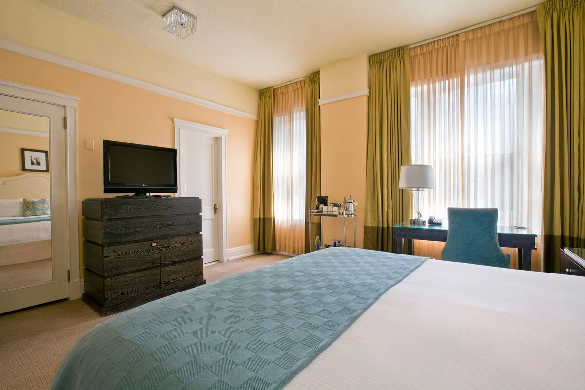 Habitación de hotel con una cama grande, cómoda, televisor, escritorio con lámpara y ventana con cortinas.