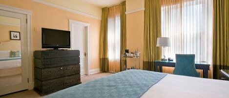 Habitación de hotel con una cama grande, cómoda, televisor, escritorio con lámpara y ventana con cortinas.